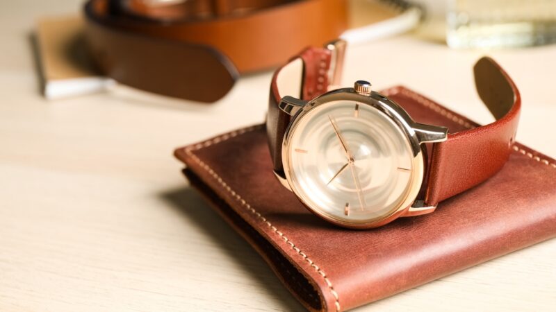 A leather watch rests on a wallet beside men’s accessories