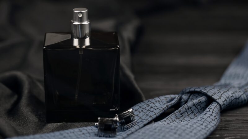 A black cologne bottle sits beside a folded blue tie