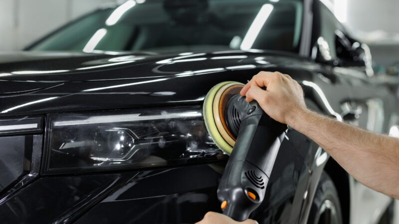 A mechanic polishes the headlight of a black car