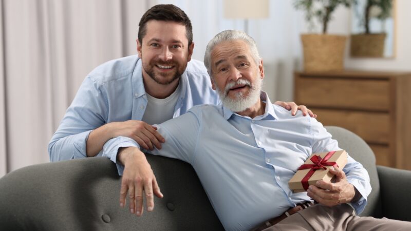 A man smiles beside an older man holding a small wrapped gift