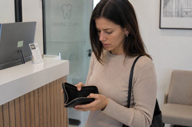 Woman holding an open wallet at a dentist’s reception desk.