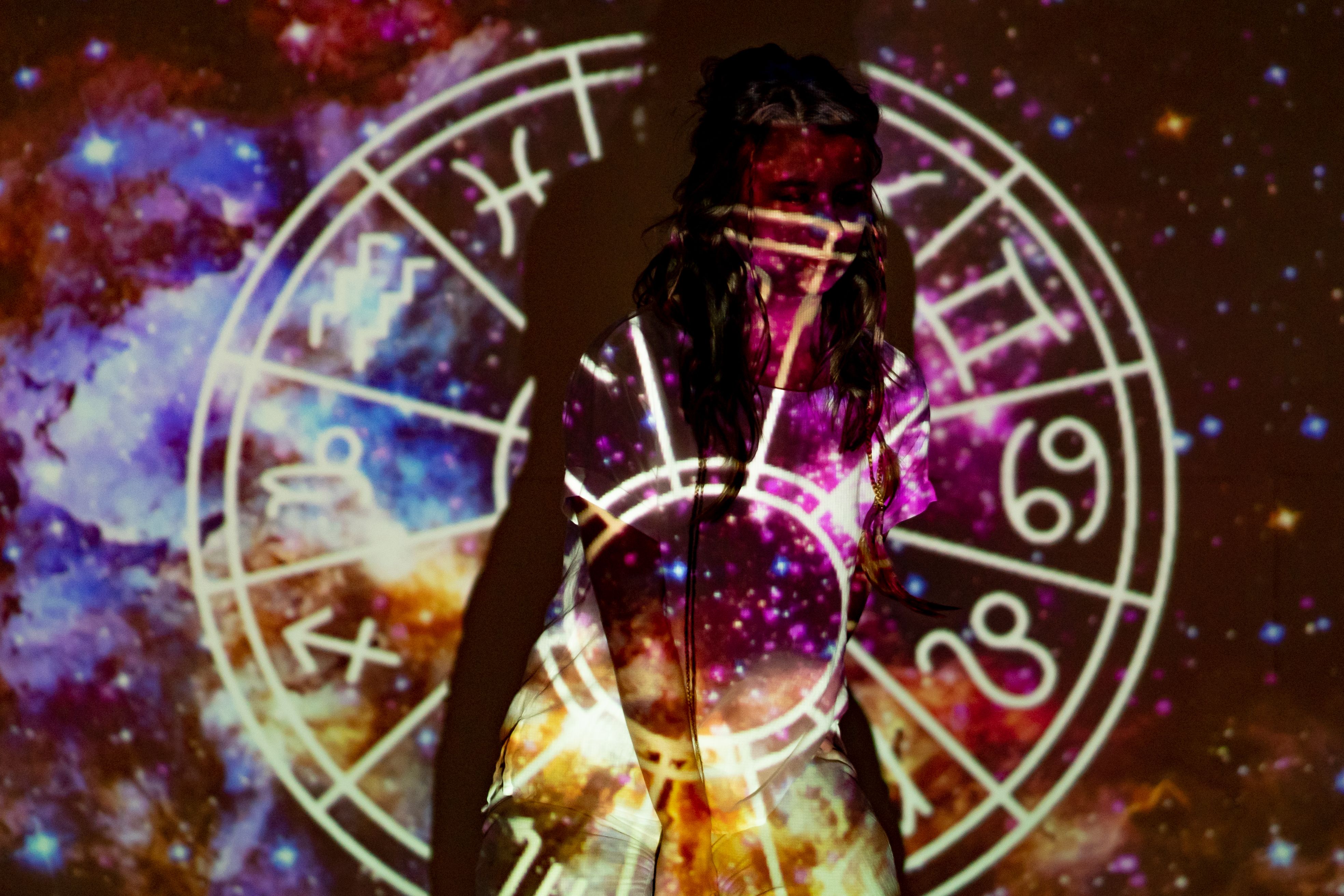 Woman surrounded by projected celestial imagery and astrological symbols
