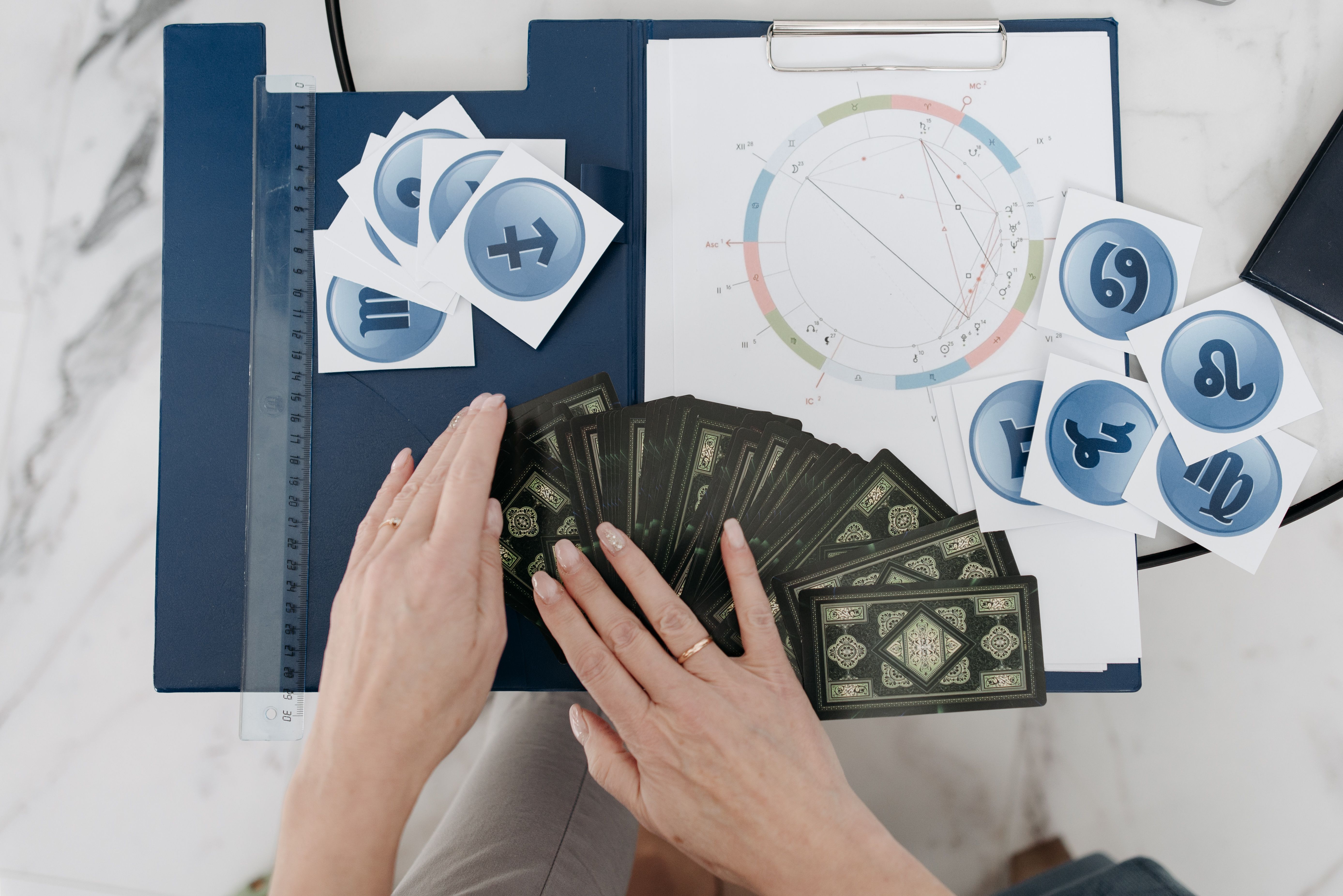 Hands arranging tarot cards beside an astrology natal chart